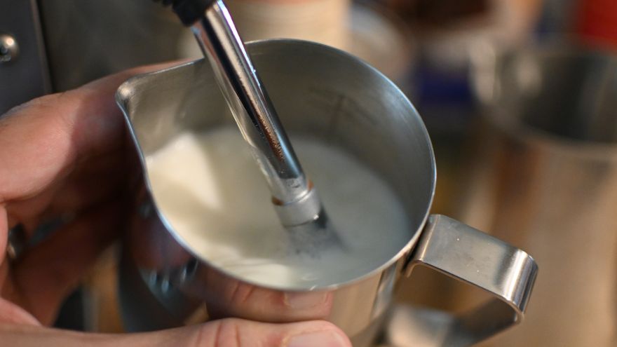 Barista spienia mleko spieniaczem ekspresowym w kawiarni