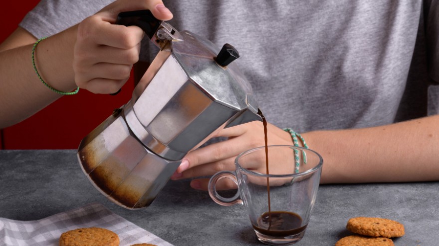 Baristka przelewa zaparzoną kawę z kawiarki do szklanki obok ciastek