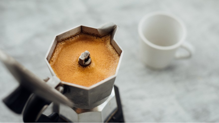 Świeżo parzona kawa w kawiarce z kubkiem do espresso obok na stole